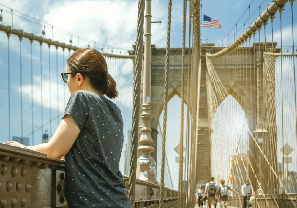 Woman with sunglasses looking cityscape from Brooklyn Bridge with Manhattan skyline on background, in New York City